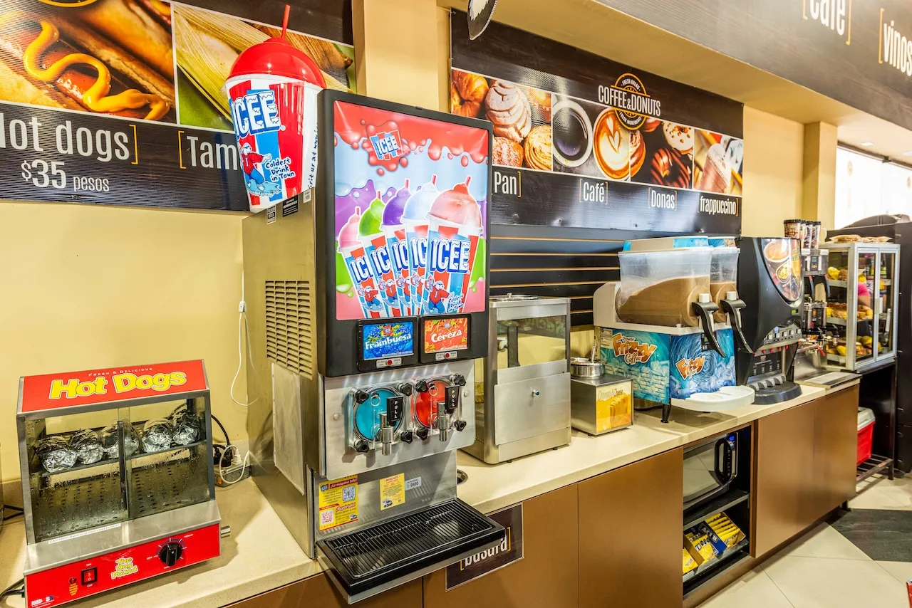 Máquina dispensadora de bebidas ICEE y estufa con hot dogs en mostrador de tienda de conveniencia.
