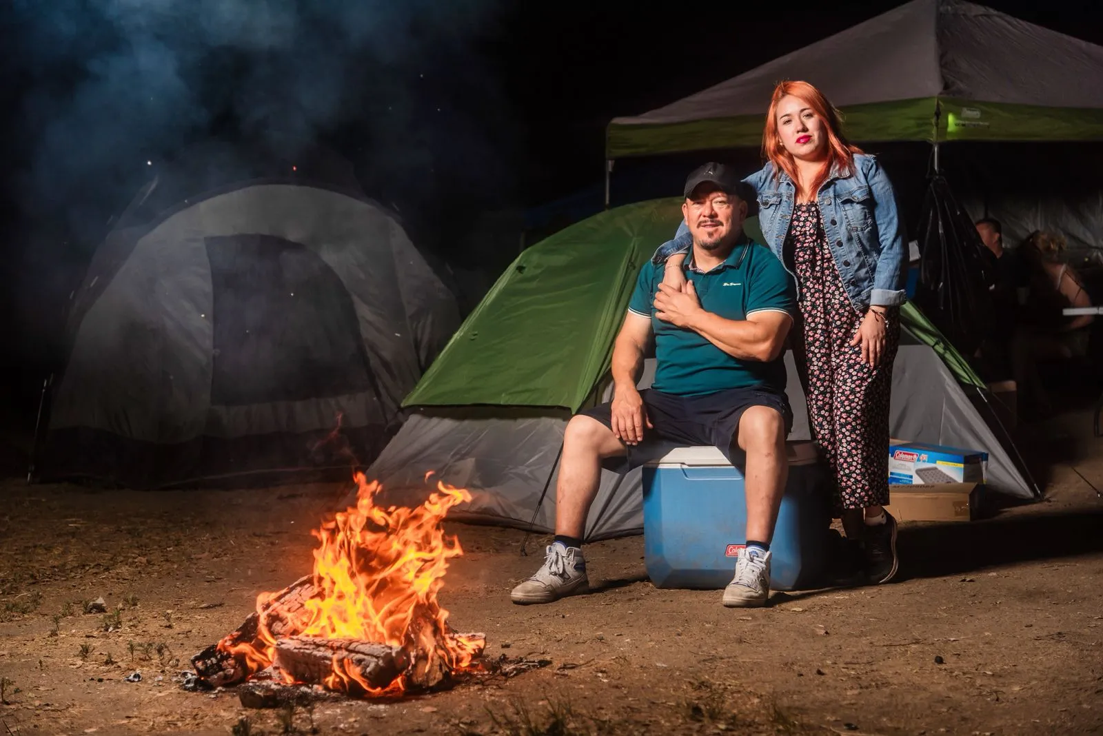 Pareja junto a una fogata y tiendas de campaña durante una acampada nocturna.