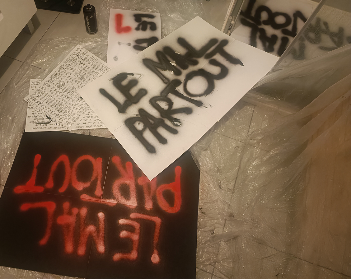 Several sheets of paper and cardboard with the phrase 'LE MAL PARTOUT' spray-painted in black and red, scattered on a plastic-covered floor.