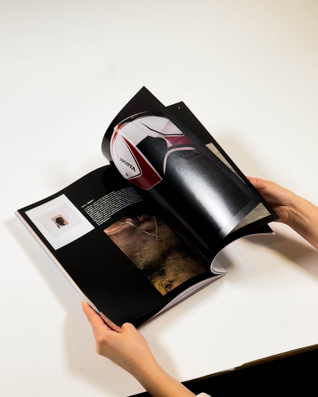 Person turning the page of a magazine with a photo of a red and white helmet and an image of a necklace on a glittery chest.