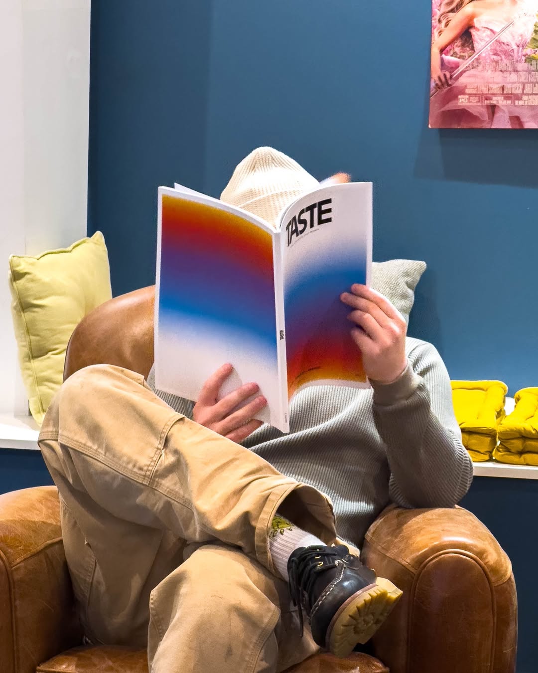 Person sitting in a brown leather armchair reading a magazine titled 'TASTE' with colorful gradient cover.