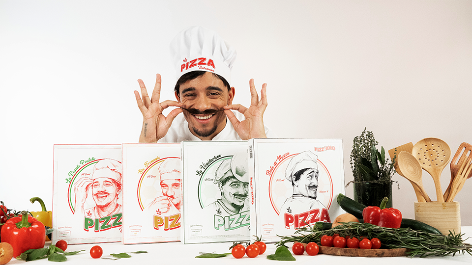 Smiling chef wearing a white hat labeled 'Pizza' playfully holding his mustache surrounded by pizza boxes, fresh vegetables, and herbs.