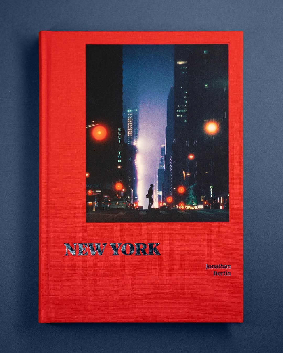 Red hardcover book titled 'NEW YORK' with a nighttime city street photo showing silhouette of a person and illuminated buildings.