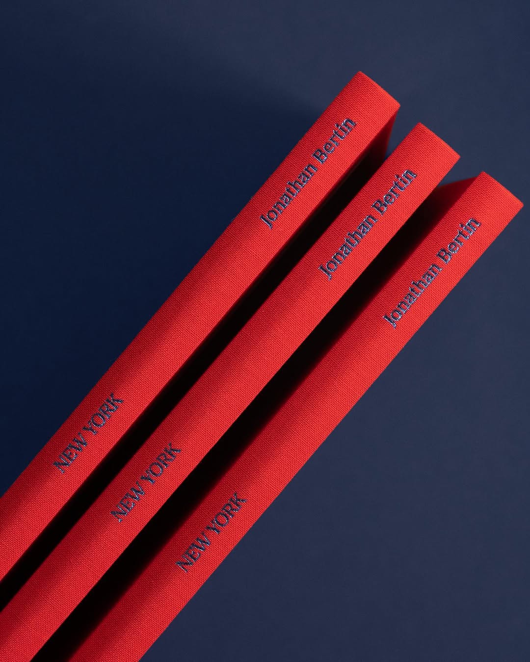 Three red hardcover books with navy text reading 'NEW YORK' and 'Jonathan Bertin' on their spines, arranged diagonally on a dark blue background.