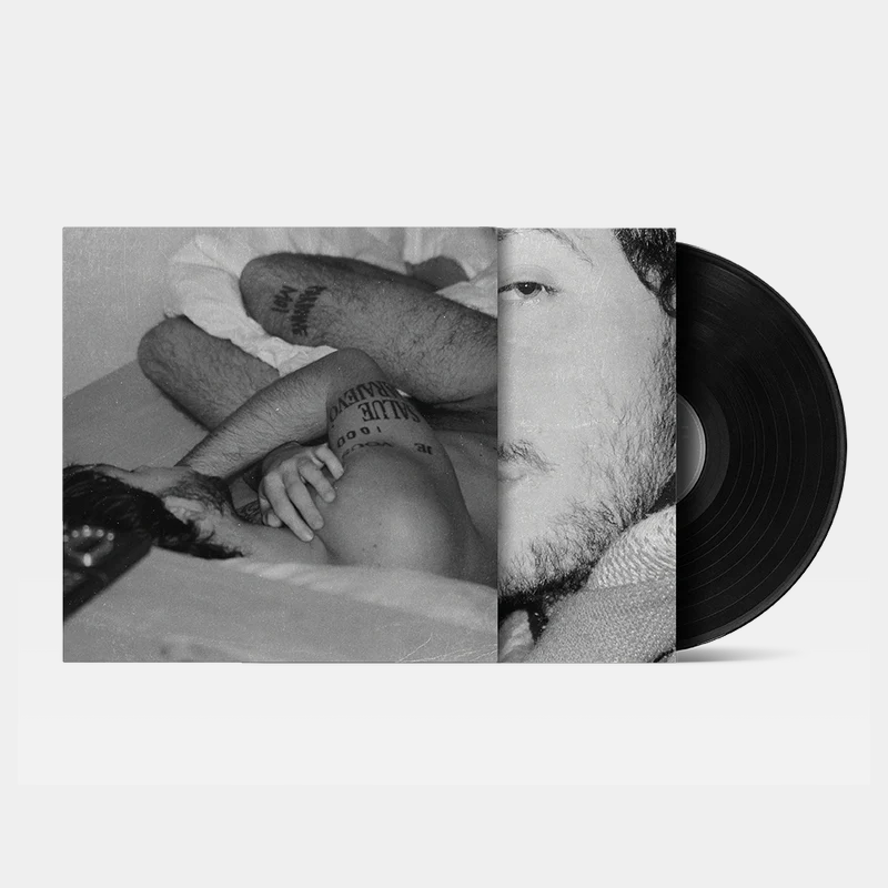 Black and white photo of a shirtless man lying down with visible tattoos, featured on a vinyl record cover partially showing the man's face.