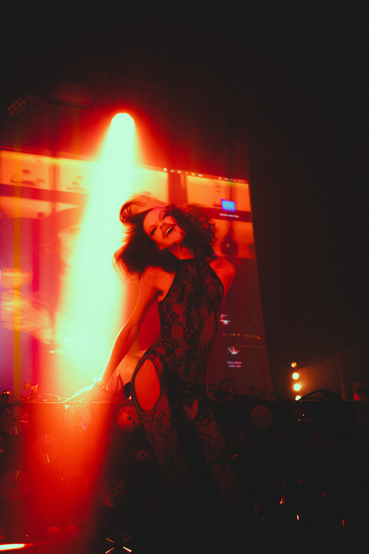 Woman dancing energetically in black lace outfit under red and orange stage lighting.