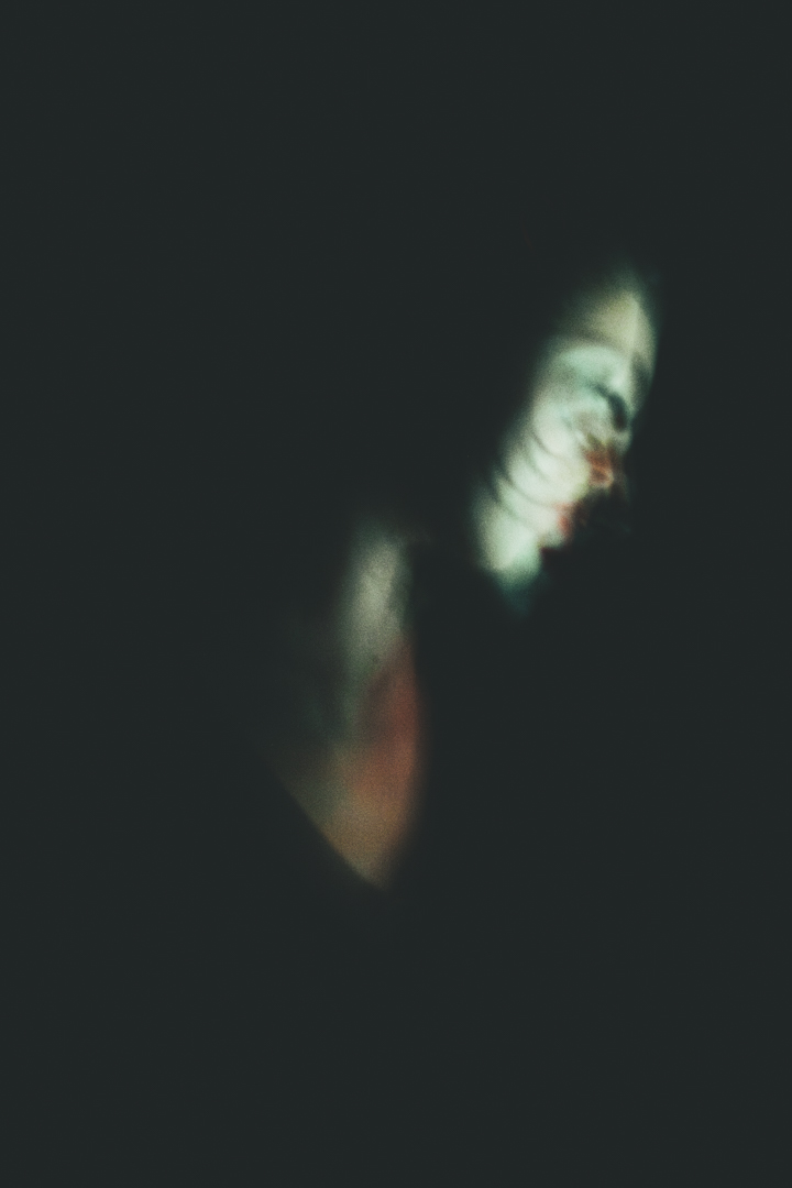 Blurred, ghostly profile of a person with green and red tones against a dark background.