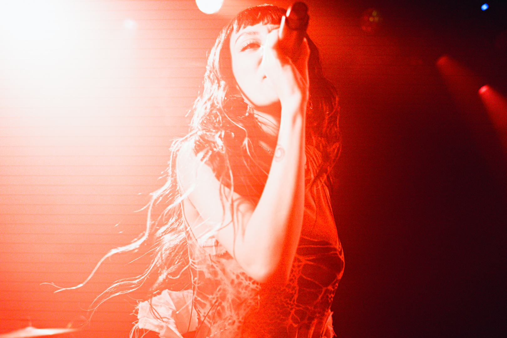 Female singer with long hair holding a microphone passionately performing on stage under red lighting.