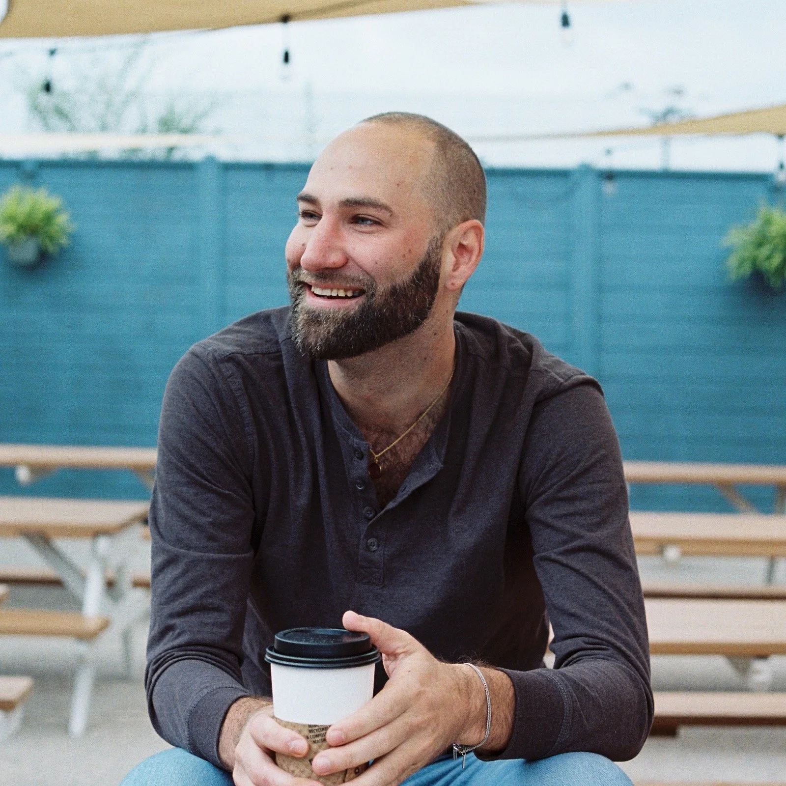 KBS co-owner sitting outdoors with a coffee, smiling during a business meeting.