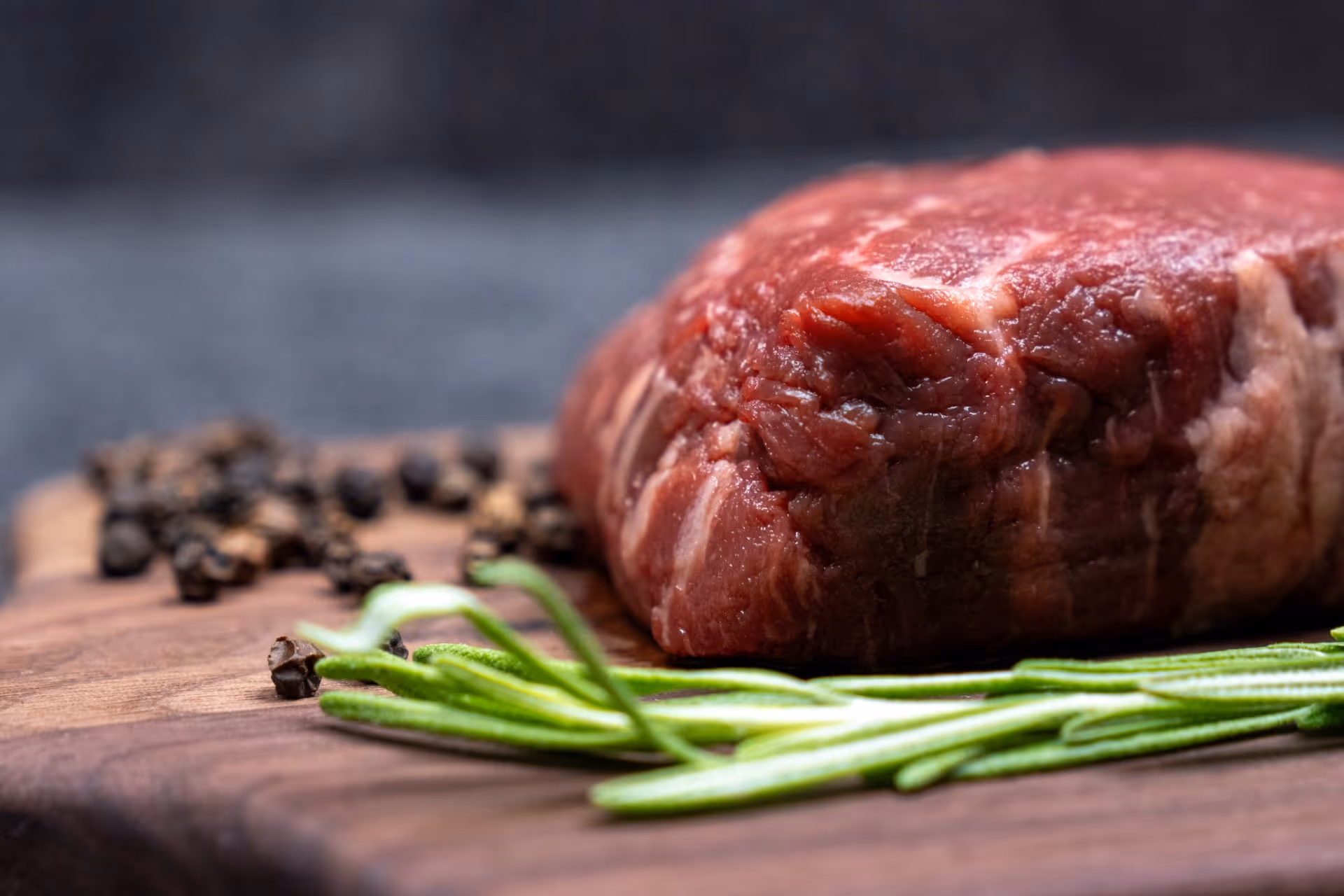Raw beef steak with rosemary and black pepper on wooden board
