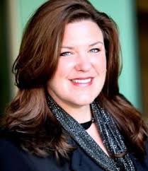 Portrait of a smiling woman with long brown hair wearing a black top and a glittery scarf.