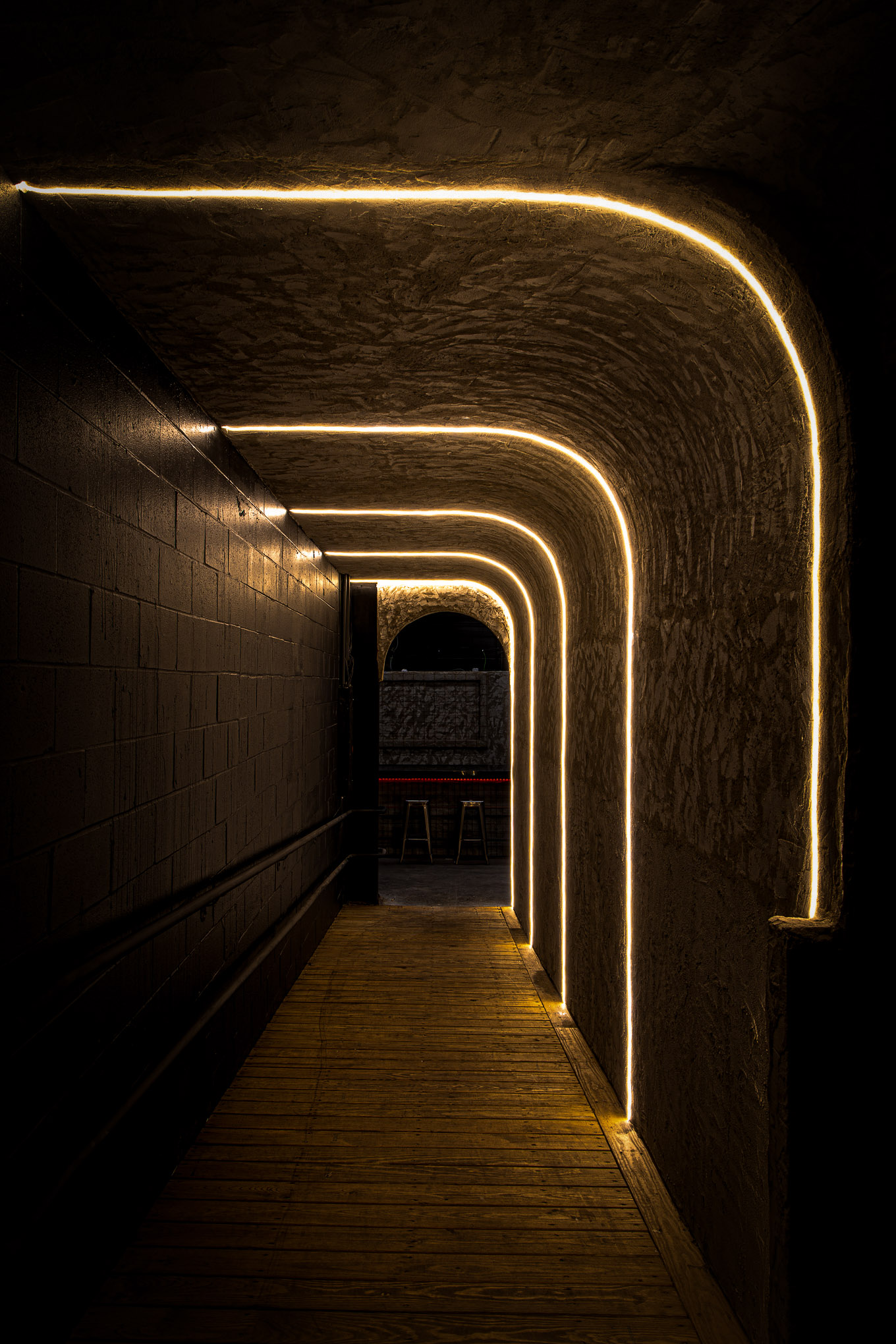 Dimly lit narrow corridor with curved ceiling and walls outlined by warm yellow LED strip lights.