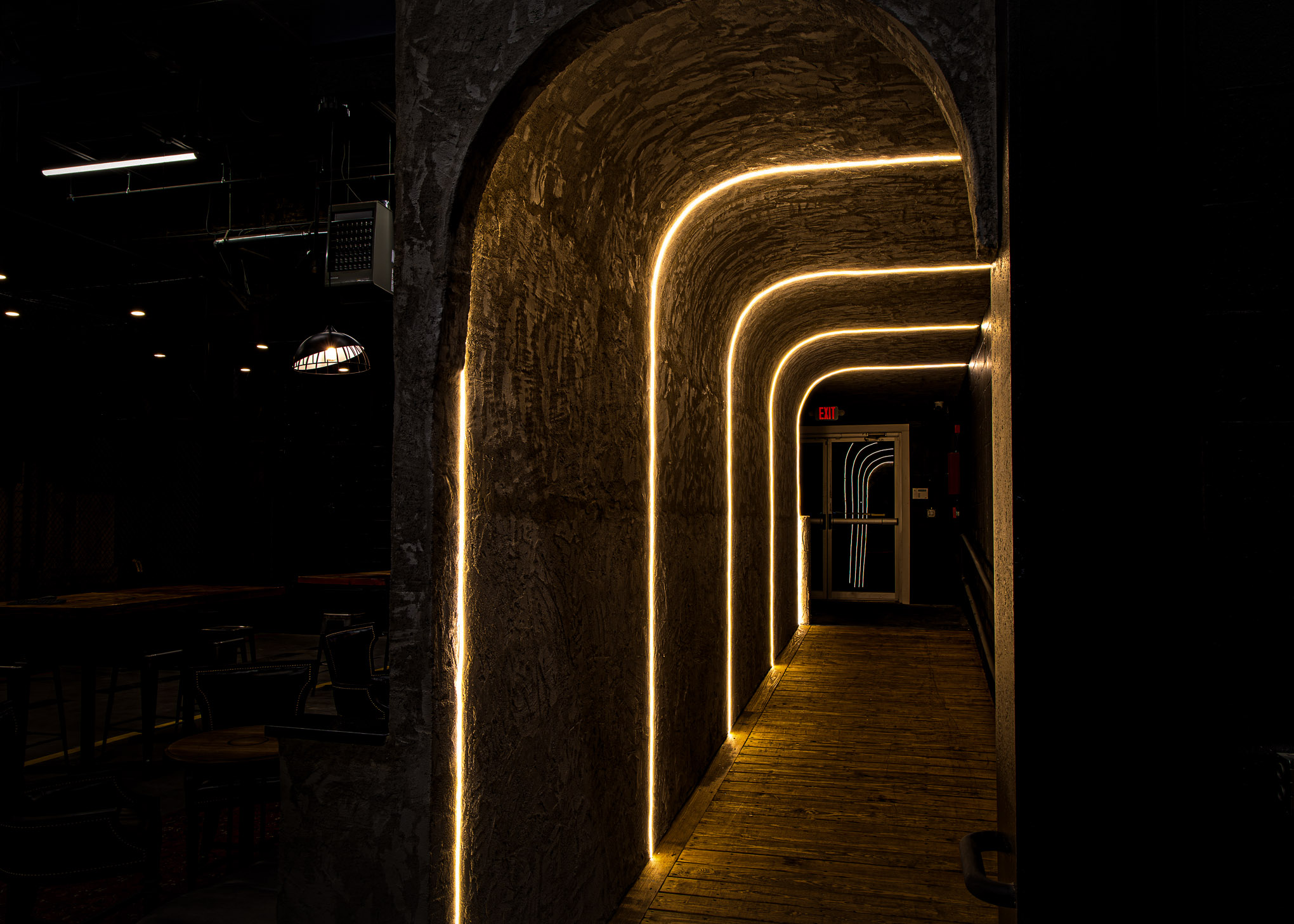 Dimly lit arched hallway with warm yellow LED strip lights outlining the walls and ceiling leading to an exit door.