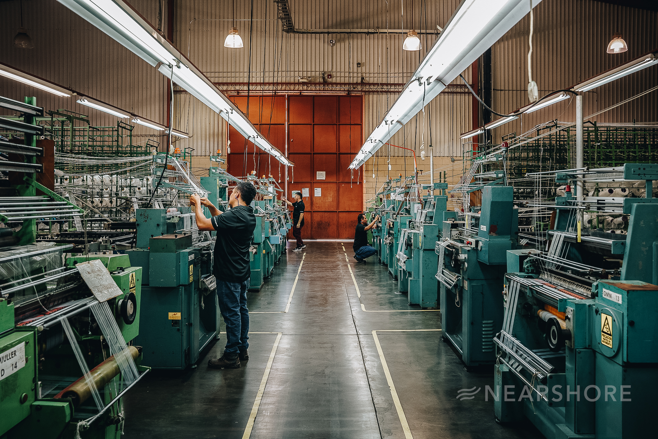 Cut-and-sew factory materials including fabric rolls, thread spools, and tailoring scissors on a worktable, representing textile manufacturing and fabric sourcing.