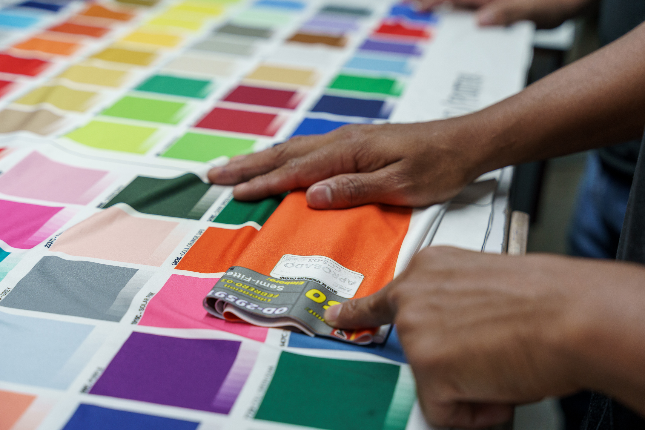 Cut-and-sew factory materials including fabric rolls, thread spools, and tailoring scissors on a worktable, representing textile manufacturing and fabric sourcing.