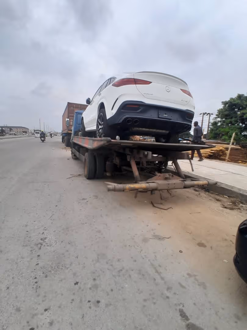 White Mercedes-Benz SUV loaded on a flatbed tow truck on the side of a road.