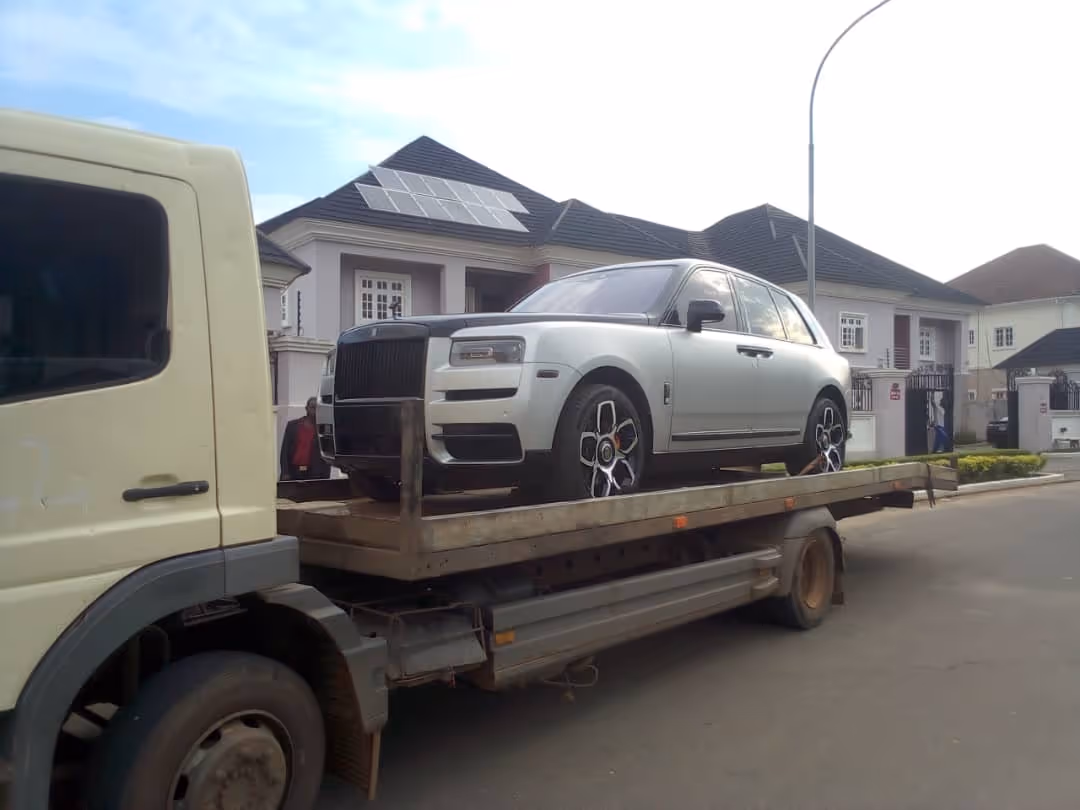 Silver luxury SUV loaded on the bed of a flatbed tow truck parked on a residential street.