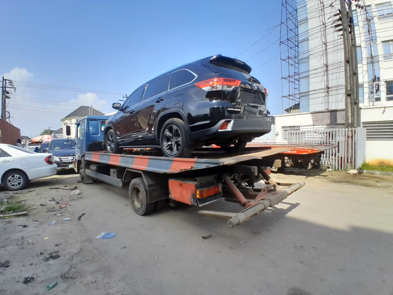 Black SUV loaded on a flatbed tow truck parked on a street in an urban area.