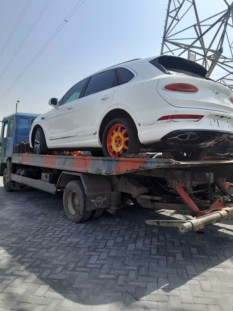 White SUV with a red spare wheel on a flatbed tow truck under a clear sky.