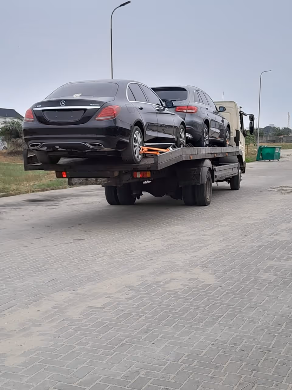 Two black Mercedes-Benz vehicles secured on the back of a flatbed tow truck on a paved road.