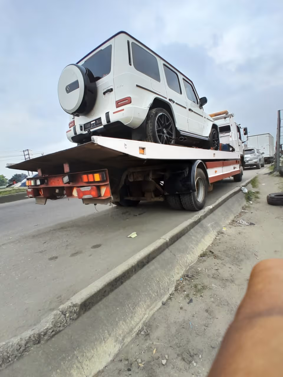 White SUV loaded on the back of a flatbed tow truck parked on a roadside curb.