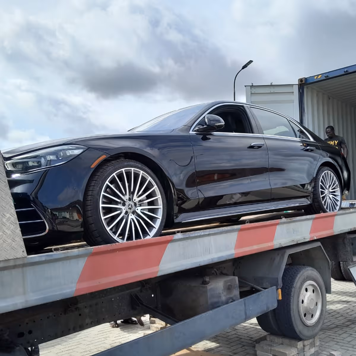 Black luxury sedan with detailed alloy wheels loaded on a flatbed truck with a person standing nearby.