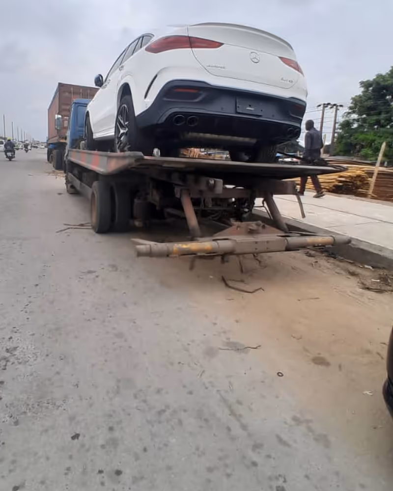 White Mercedes-Benz GLE 2024 model loaded on a flatbed tow truck on a city street.
