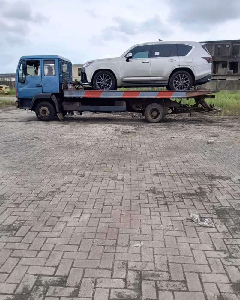 White SUV loaded on a flatbed tow truck parked on a paved surface with an overcast sky.