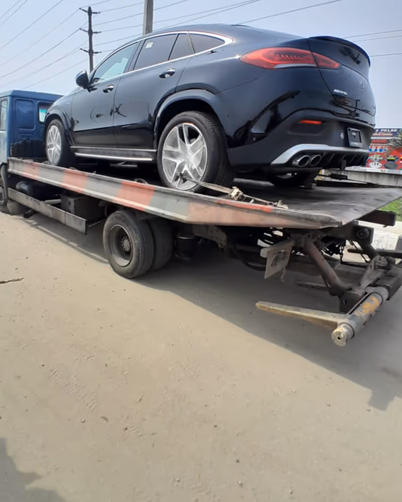 Black Mercedes-Benz SUV loaded on a flatbed tow truck on a paved road.