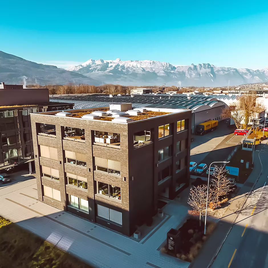 Ehemaliger Standort Triesen der Griffin Group in Liechtenstein – Luftaufnahme des Bürohauses mit Alpen im Hintergrund.