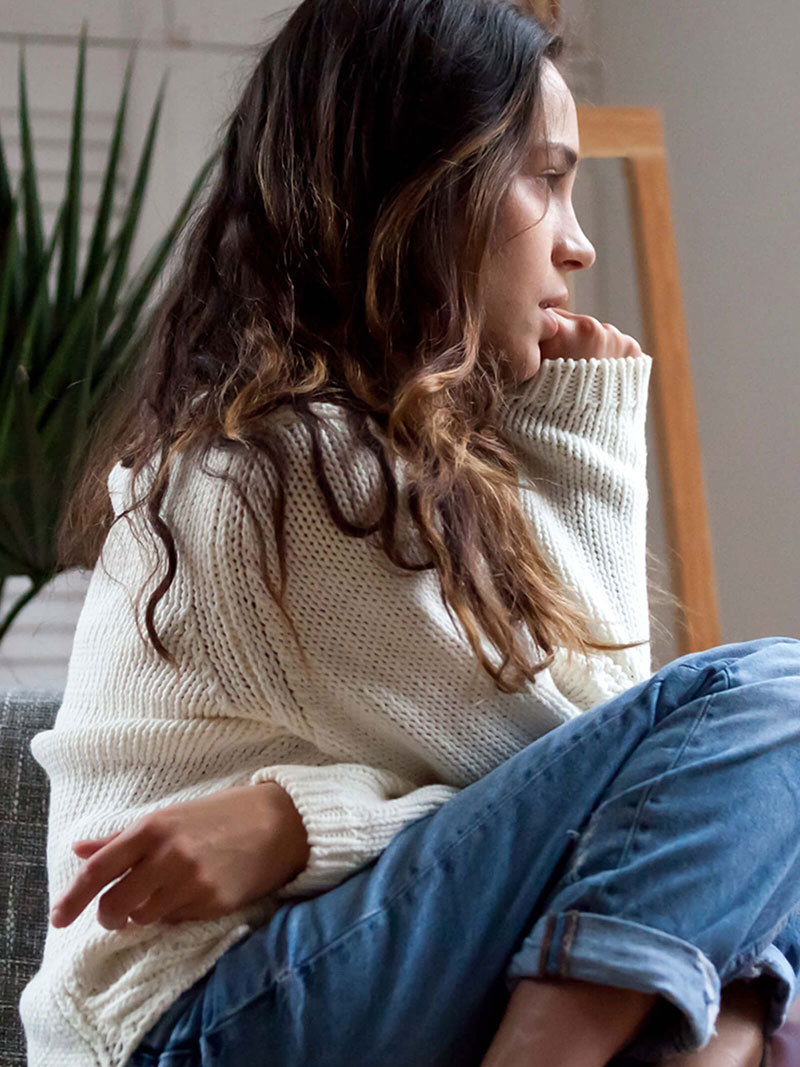 Female teenager with mental health issues sitting on a chair and looking out of a window.