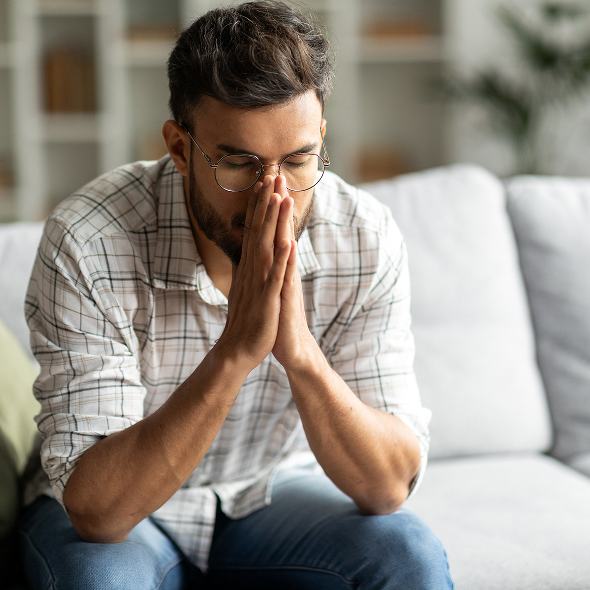 Young man with depression, sitting on a couch with folded hands.