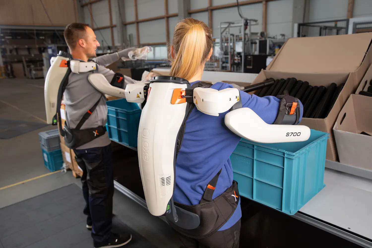Two people wearing white backpacks with robotic arms.
