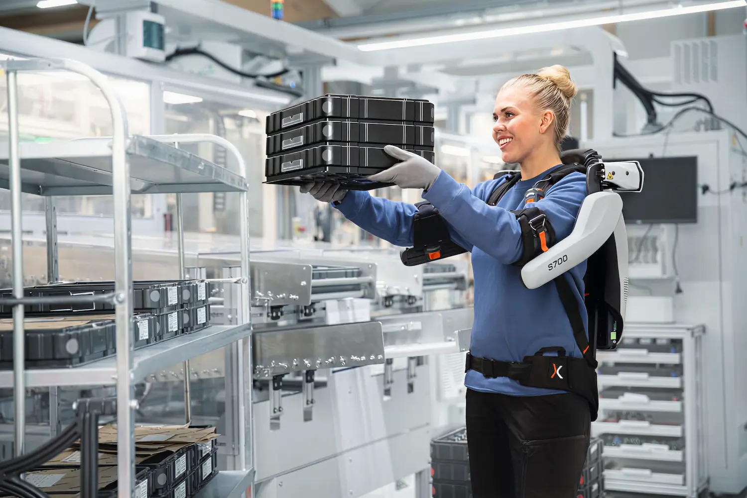A woman wearing an exoskeleton and holding a box of items.