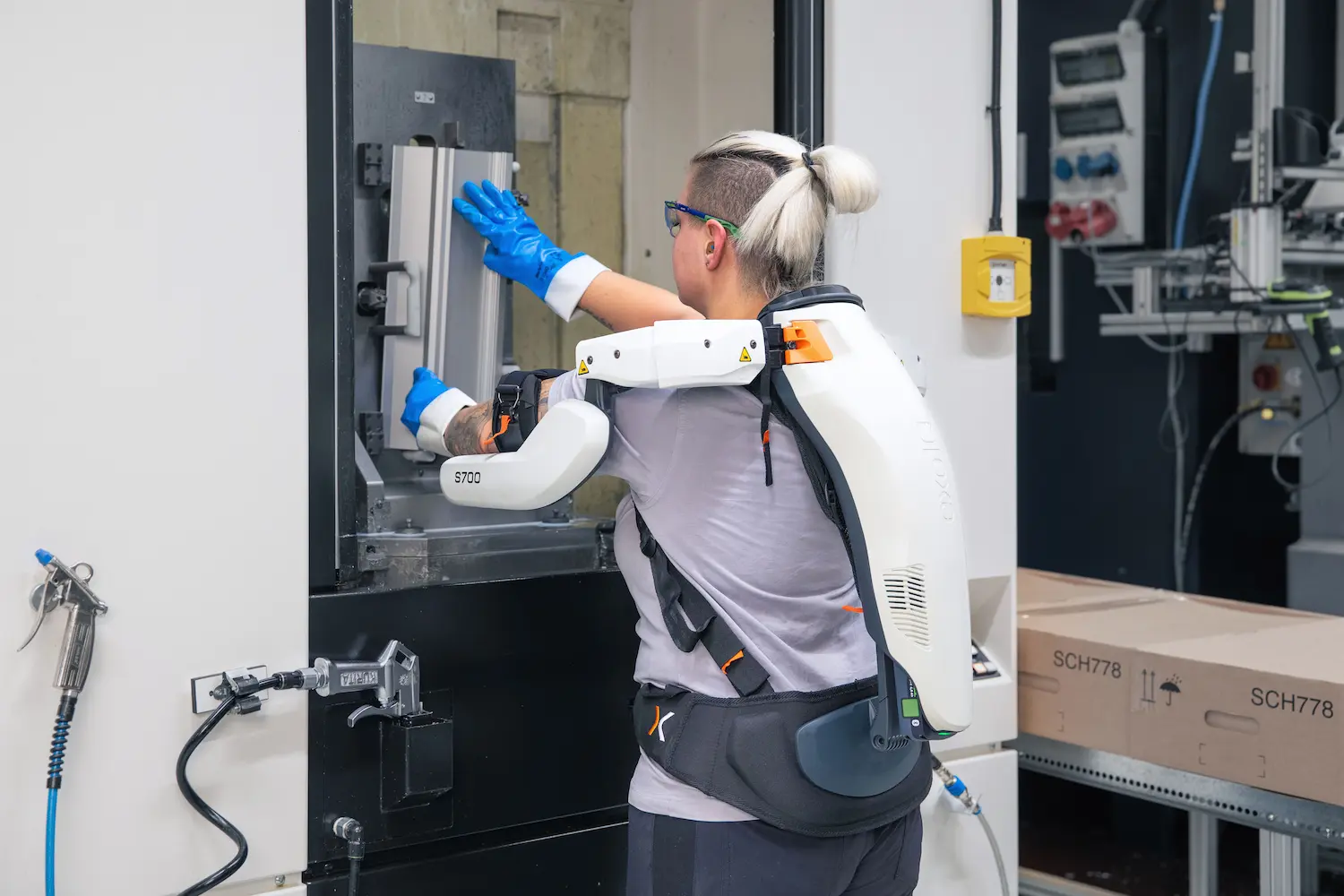 A woman wearing an exoskeleton and gloves is working in a factory.