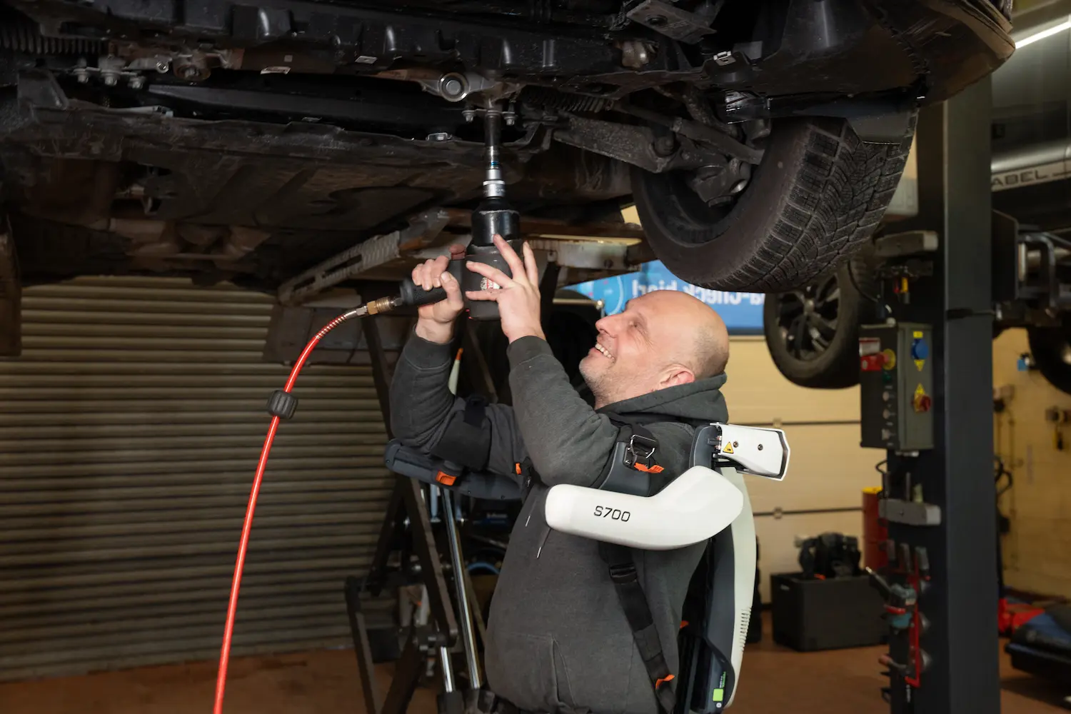 A man is working on a car in a garage with an exoskeleton.