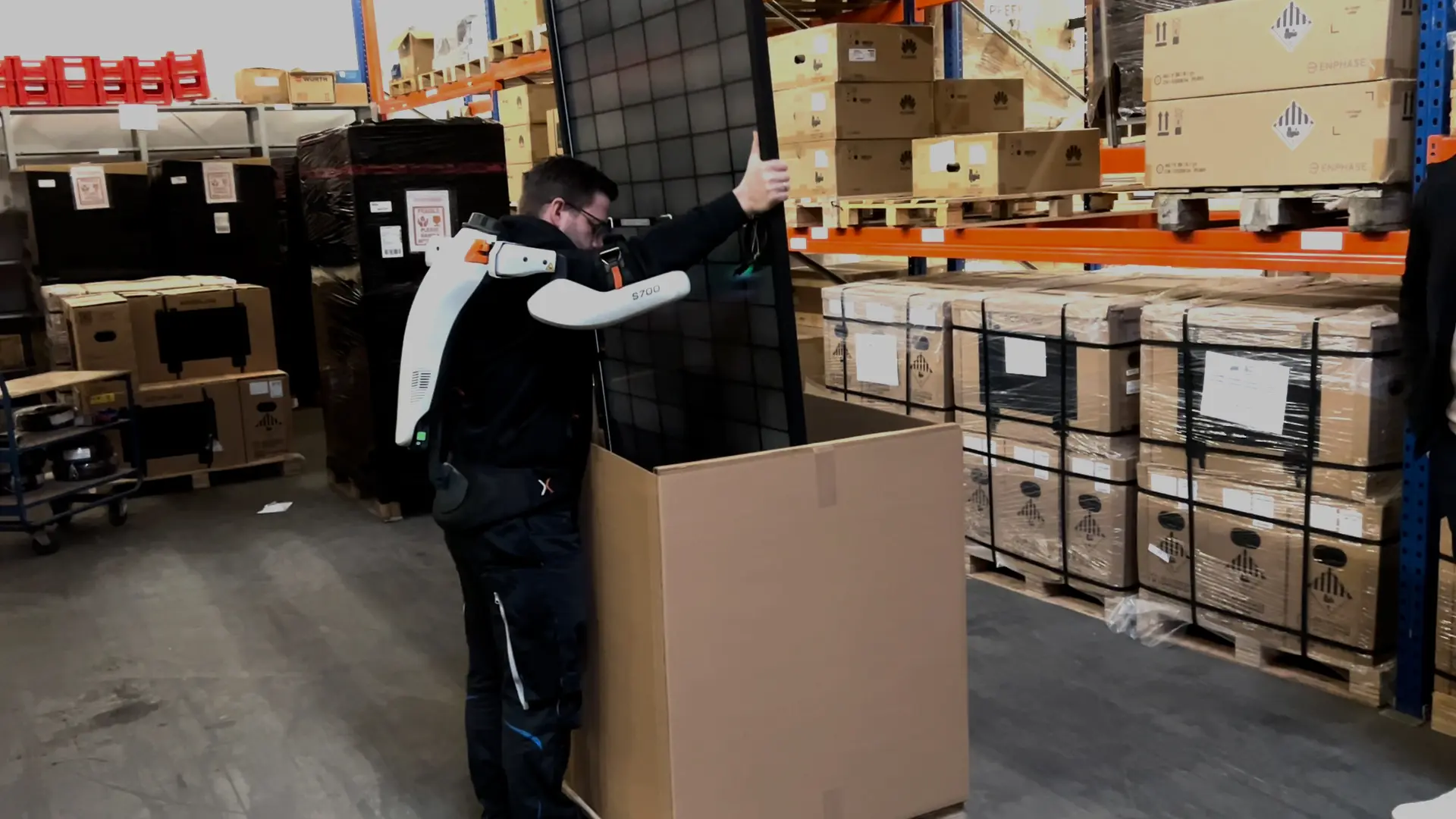 A man in a warehouse is holding a solar panel with an exoskeleton.