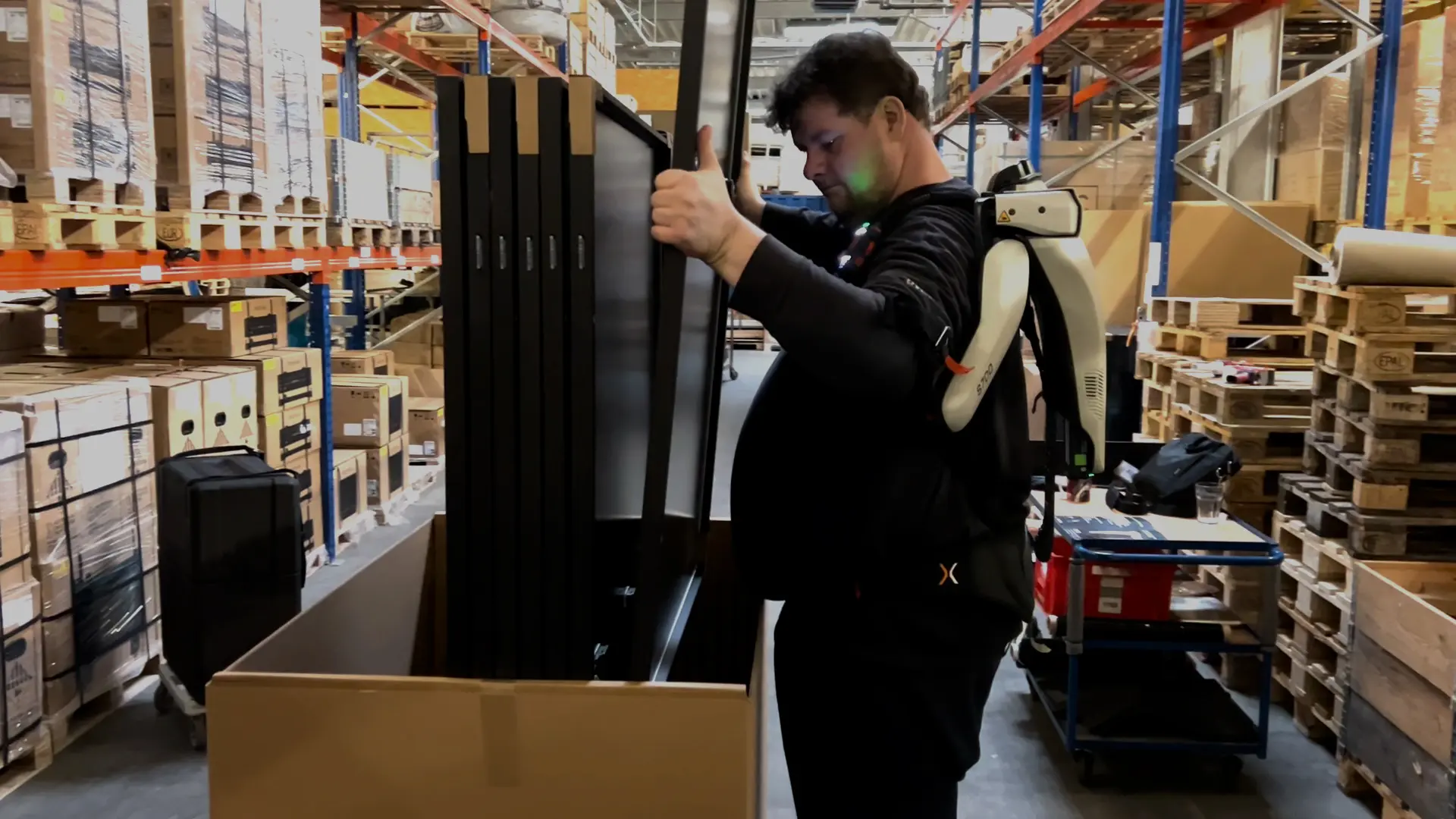 A man in a warehouse is holding a solar panel with an exoskeleton.