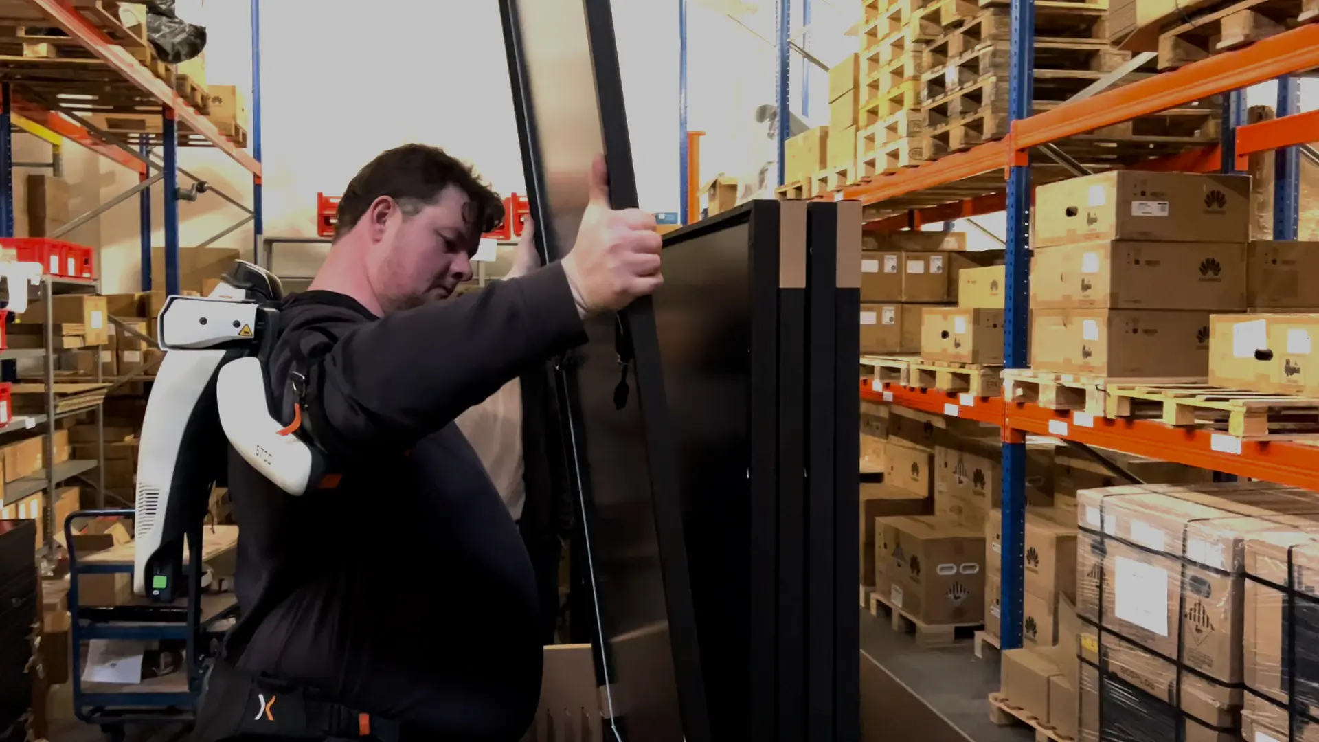 A man in a warehouse is holding a solar panel with an exoskeleton.