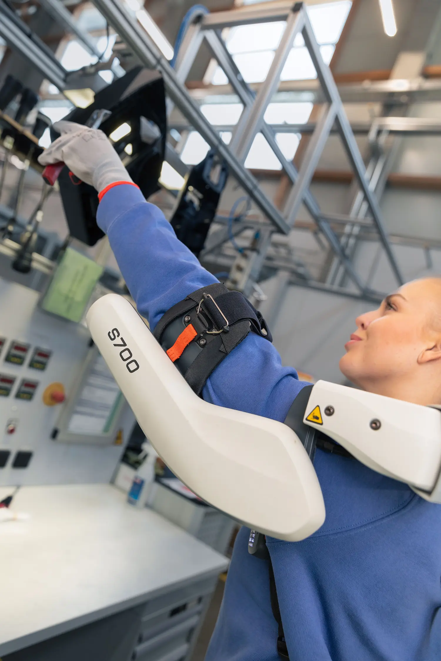 A woman wearing a blue shirt and an exoskeleton is adjusting a strap.