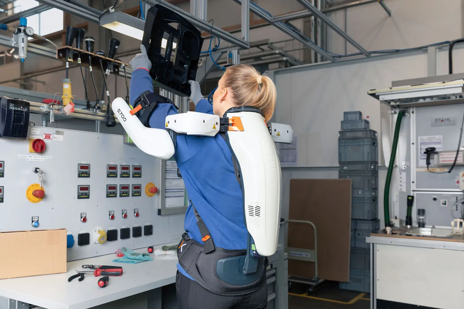 A woman wearing a blue shirt and an exoskeleton working in production.