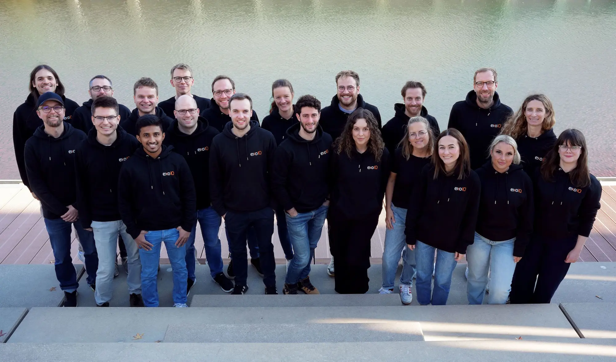 A group of people wearing black hoodies and jeans standing in front of a body of water.