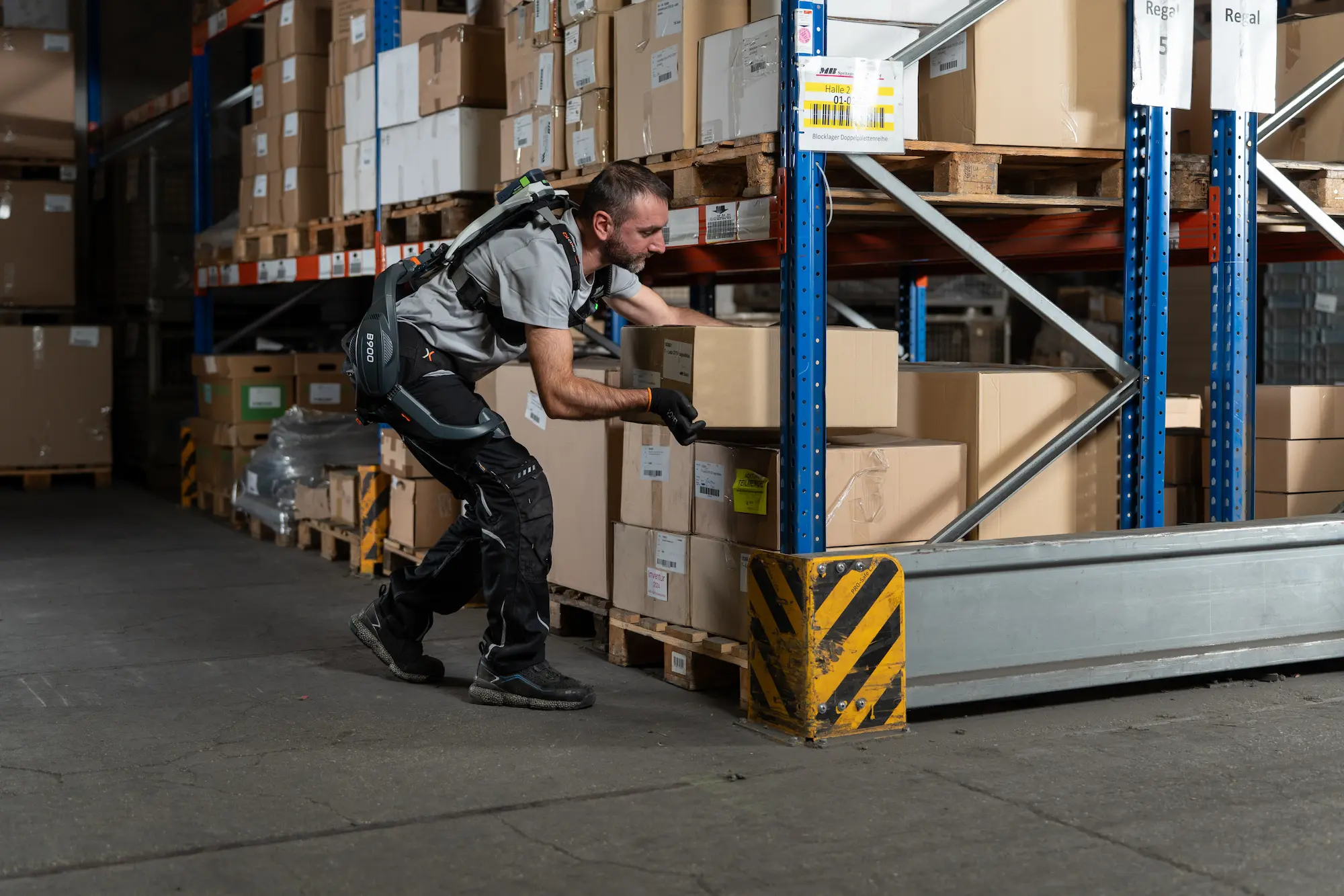 Mann mit einem aktiven Rücken-Exoskelett B900 arbeitet in einer Lagerhalle.