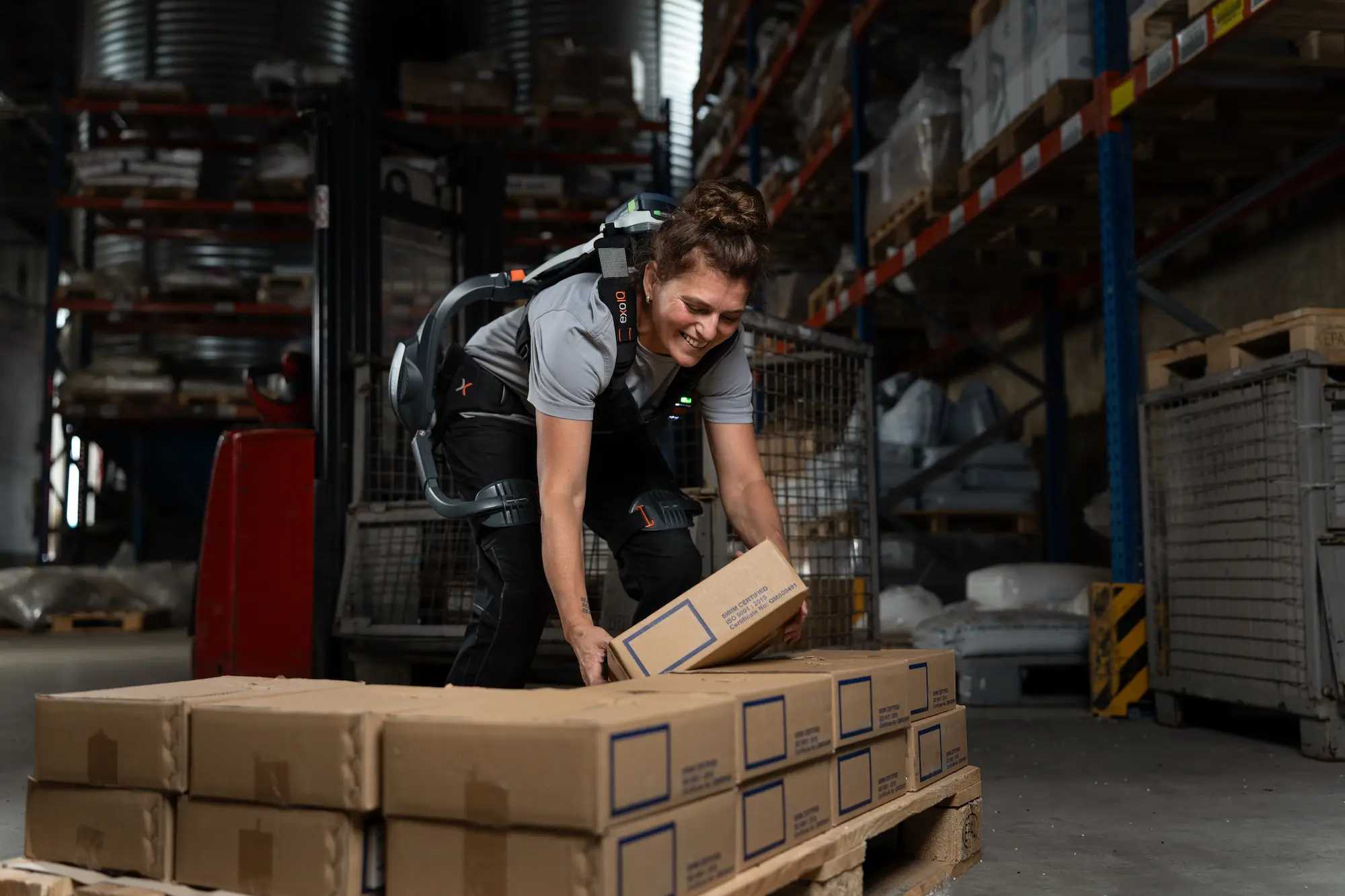 Frau mit einem aktiven Rücken-Exoskelett B900 bückt sich nach einem Karton.