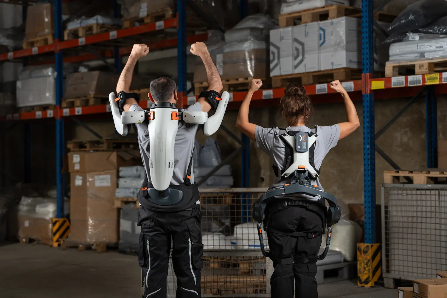 Ein Mann mit Schulter-Exoskelett und eine Frau mit Rücken-Exoskelett strecken die Arme in die Luft