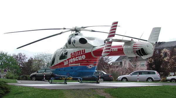 Hélicoptère moderne de secours aérien luxembourgeois posé sur une aire d’atterrissage en herbe dans une zone résidentielle.
