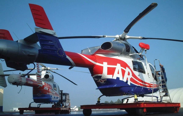 Hélicoptère Luxembourg Air Rescue avec marquage LAR sur une plateforme, un autre hélicoptère visible en arrière-plan.