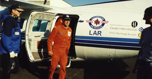 Membre d’équipage en combinaison orange sortant d’un avion Luxembourg Air Rescue portant des logos d’aide humanitaire.