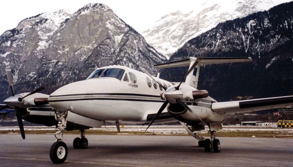 Avion bimoteur à hélices stationné sur une piste dans un paysage montagneux avec des sommets enneigés en arrière-plan.