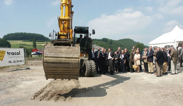 Cérémonie officielle de lancement de chantier Luxembourg Air Rescue avec pelleteuse et invités sur le site de construction.